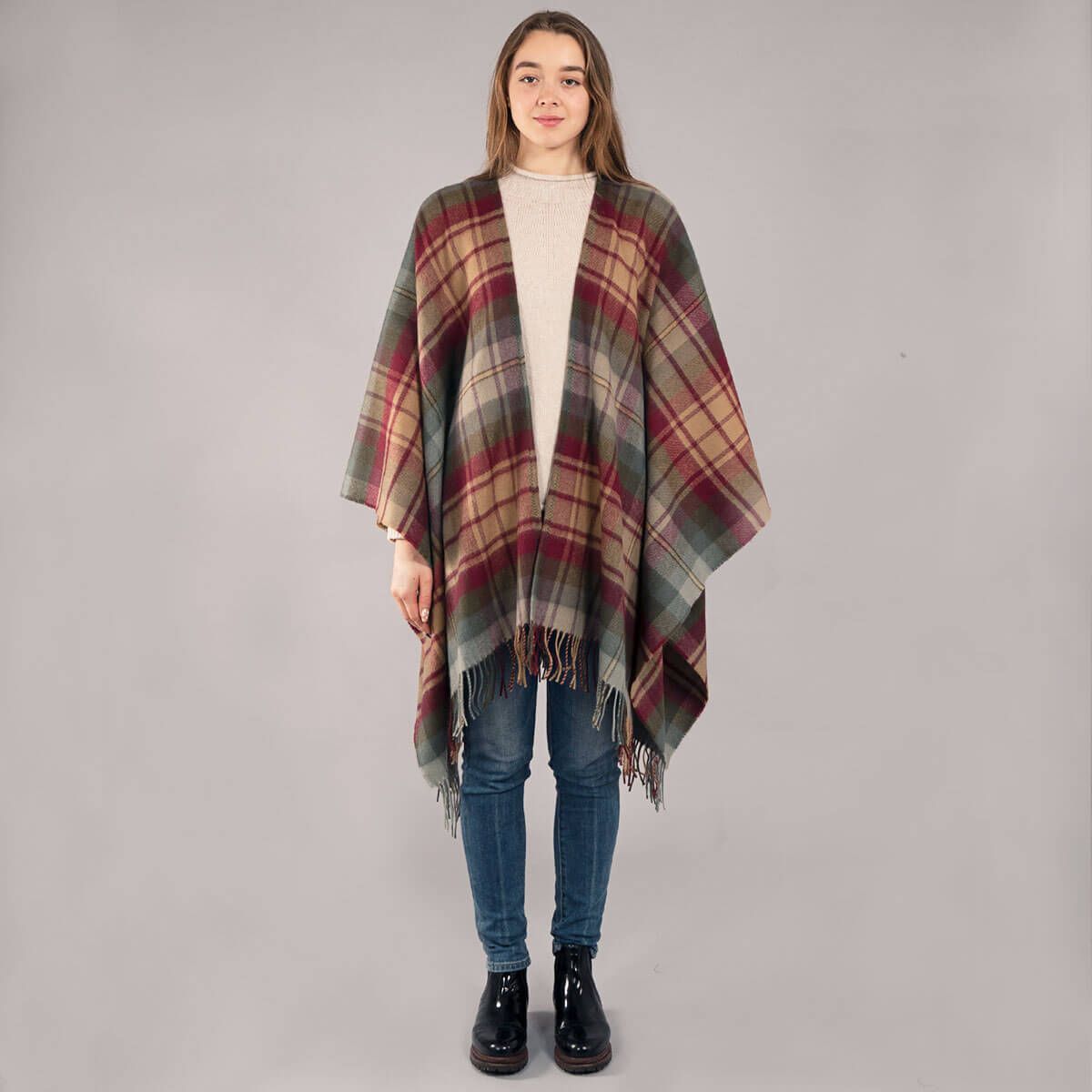 Person wearing a plaid poncho over a beige sweater and jeans on a gray background