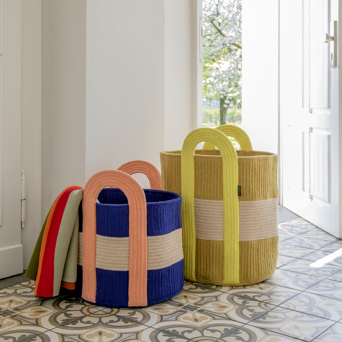 Colorful woven baskets with handles on a patterned floor.