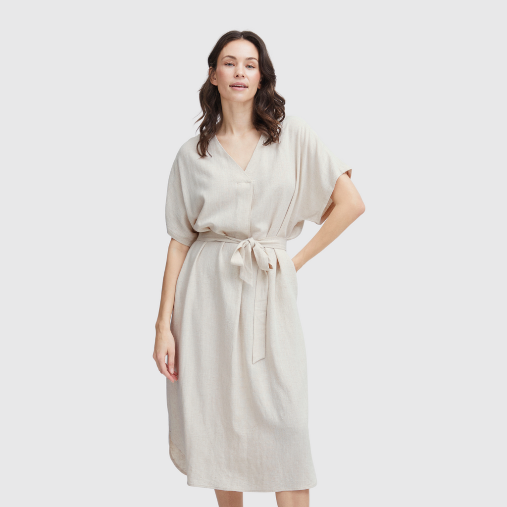 Woman in a light beige Fransa dress with short sleeves and a tie waist, smiling against a neutral background.