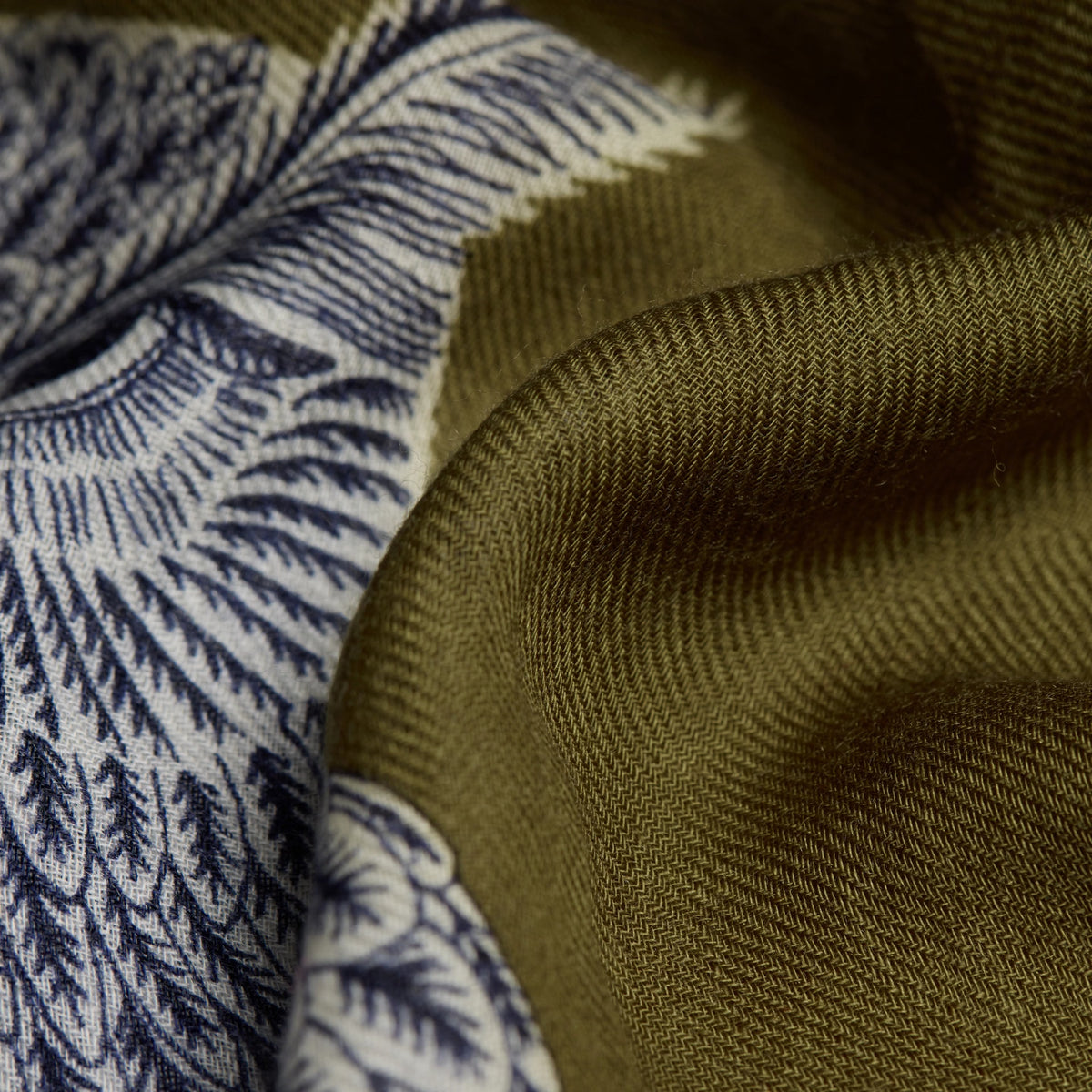 Close-up of a woven textile with a solid olive green section and a blue and off-white patterned section, showing the fabric texture and weave.