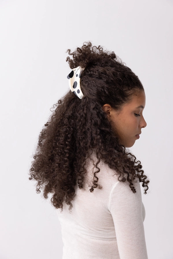 Woman with styled hair wearing a polka dot dog shaped hair clip against a white background