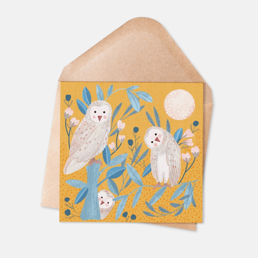 Greeting card featuring three stylized owls perched on a tree branch amidst blue foliage and flowers on a mustard yellow