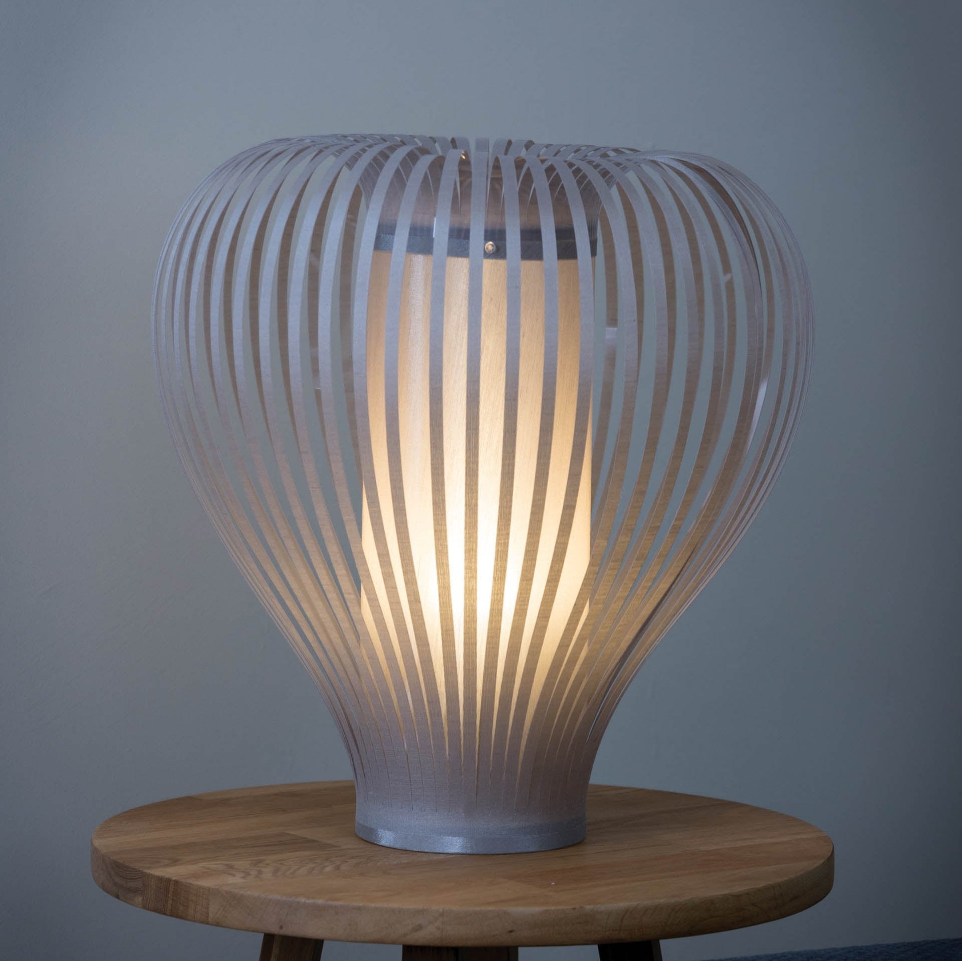 Modern table lamp with a light beige, illuminated shade composed of numerous thin, vertical strips.