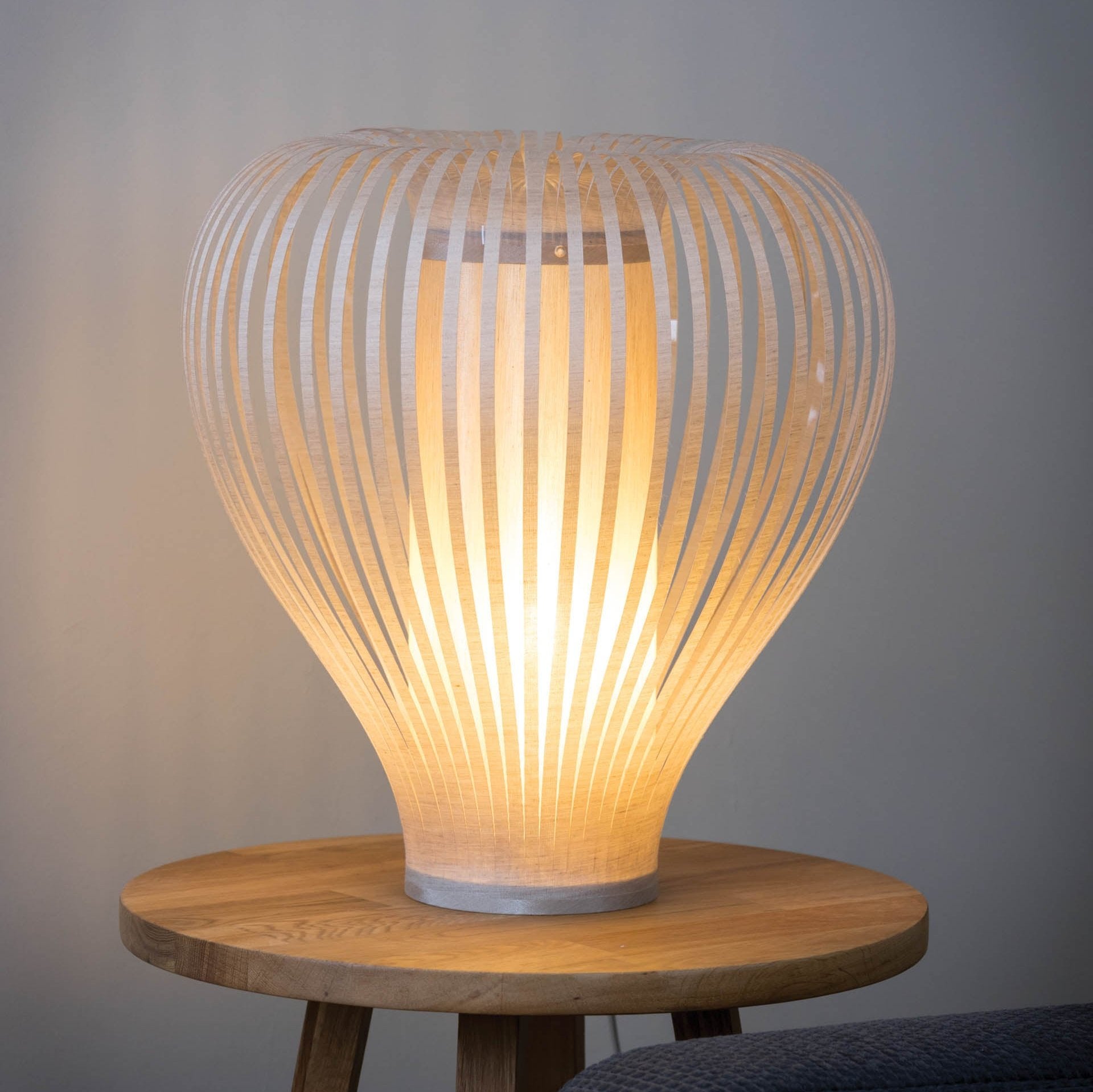 Illuminated table lamp with a light beige, curved shade composed of thin, vertical slats.