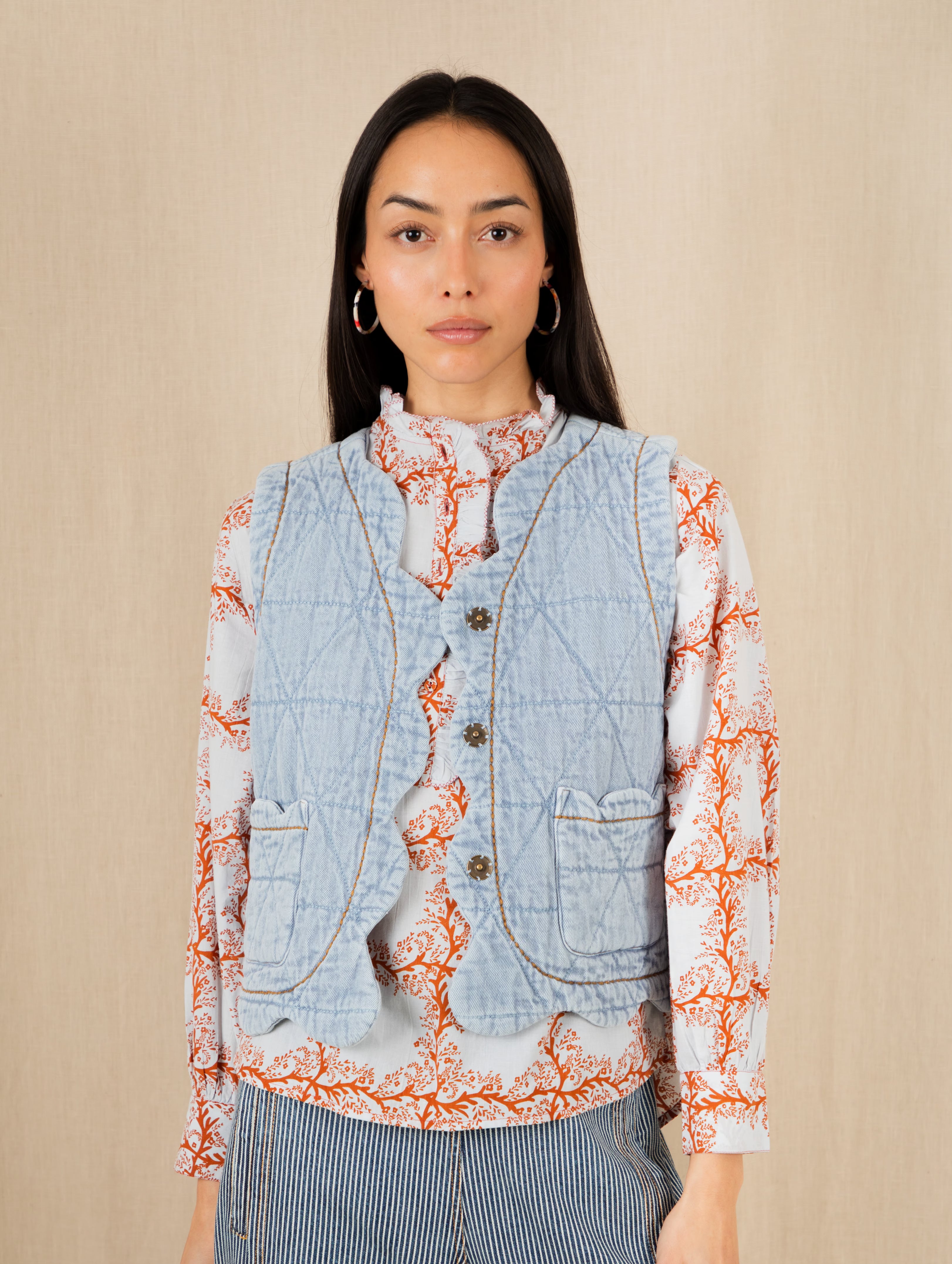 Woman wearing a denim vest over a patterned shirt on a beige background