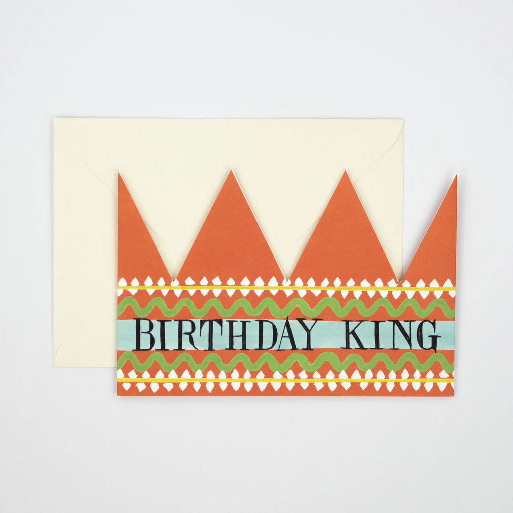 Orange paper crown with "Birthday King" text, decorated with green and yellow wavy lines and white dots, partially obscuring