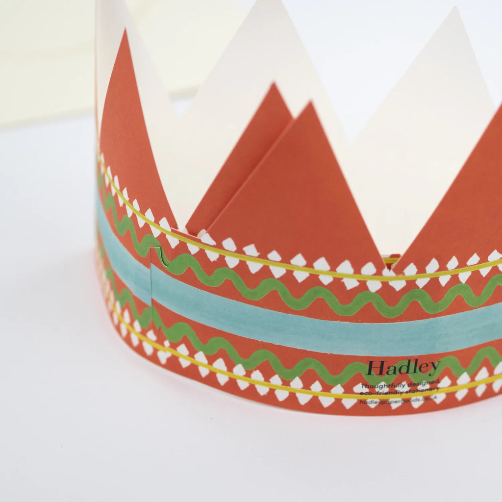 Red and white paper crown with green and teal wavy patterned band.