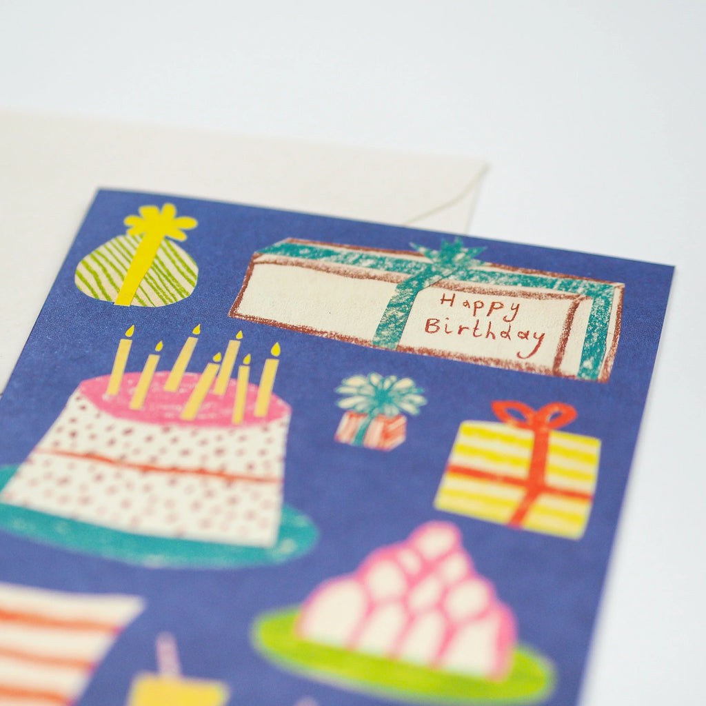 Birthday card featuring a colorful illustrated cake with candles, presents, and other celebratory imagery on a dark blue