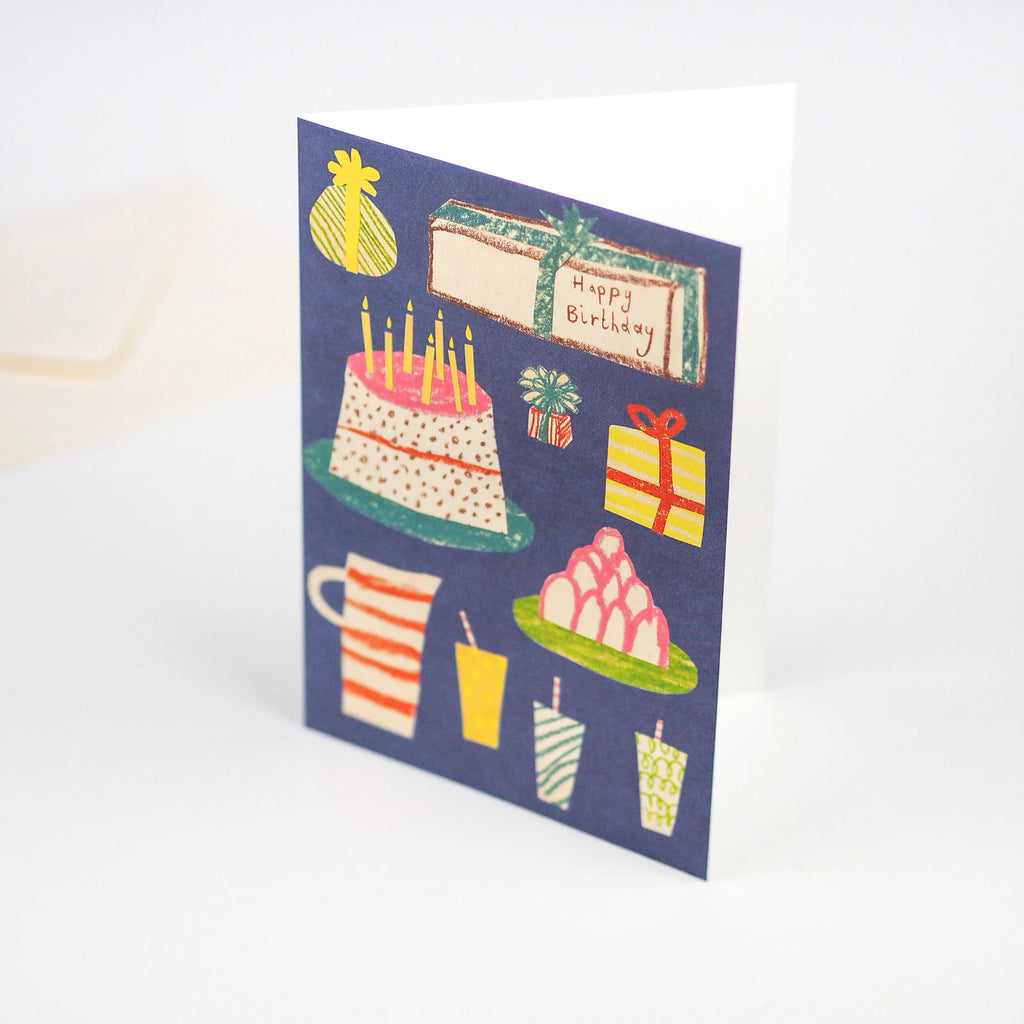 Happy birthday greeting card featuring a birthday cake, presents, drinks, and other celebratory imagery on a dark blue