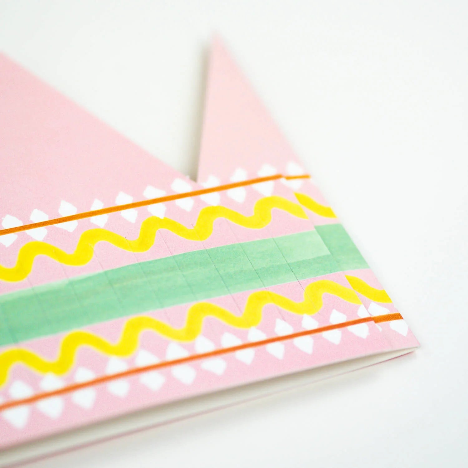 Pink paper crown with yellow, green, and orange painted stripes and white diamond shapes.