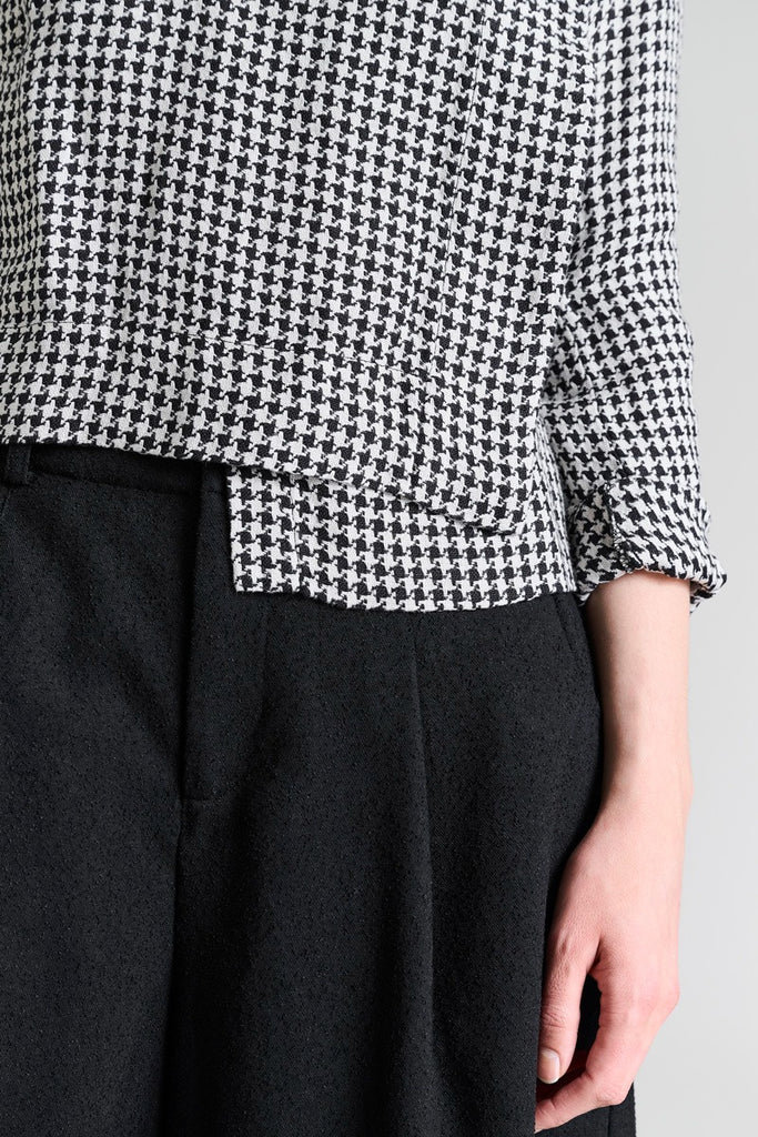 Person wearing a black and white checkered shirt with black pants on a light gray background