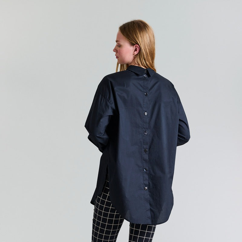 Person wearing a navy blue shirt and black checkered pants on a white background