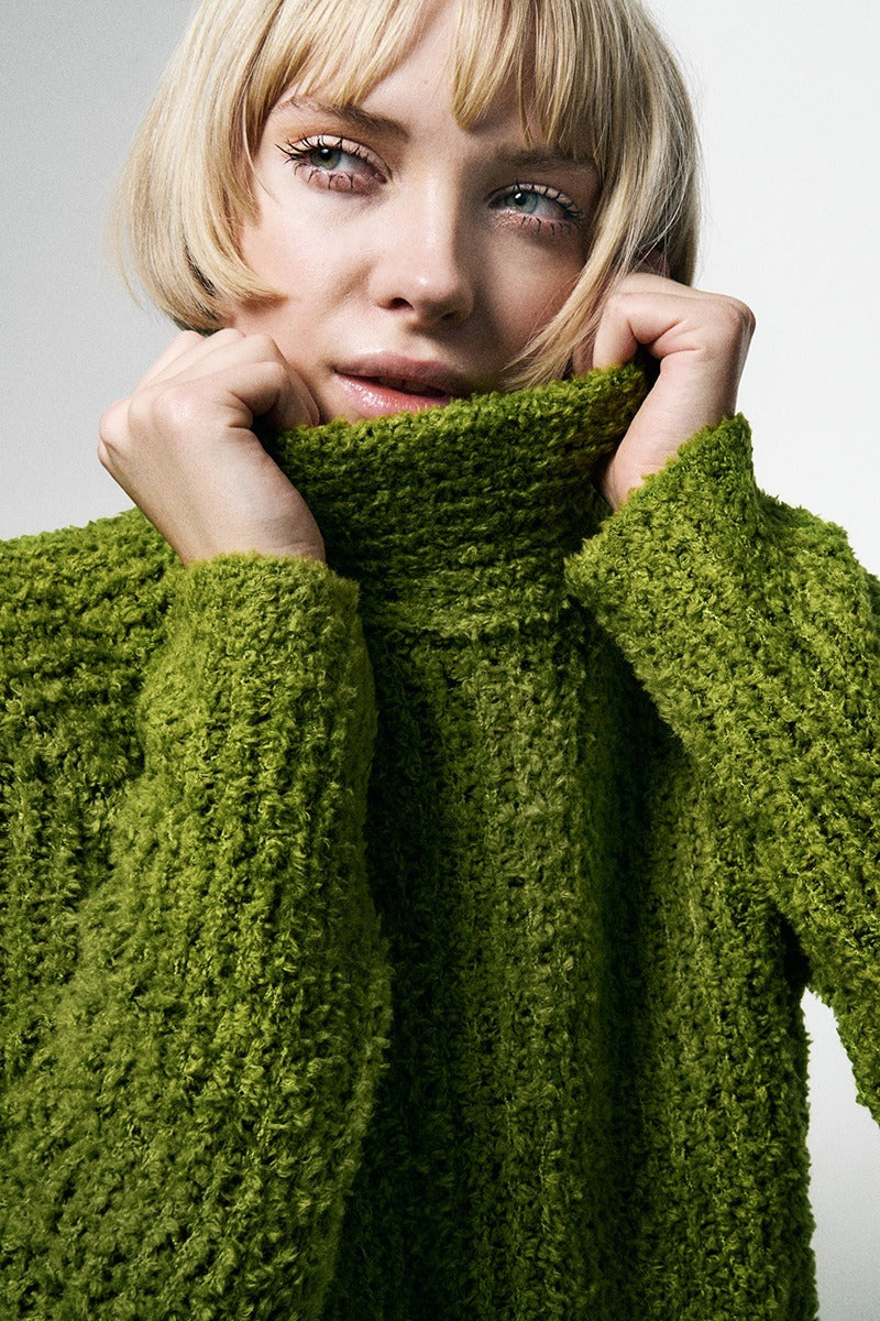 Person wearing a green knitted sweater against a neutral background