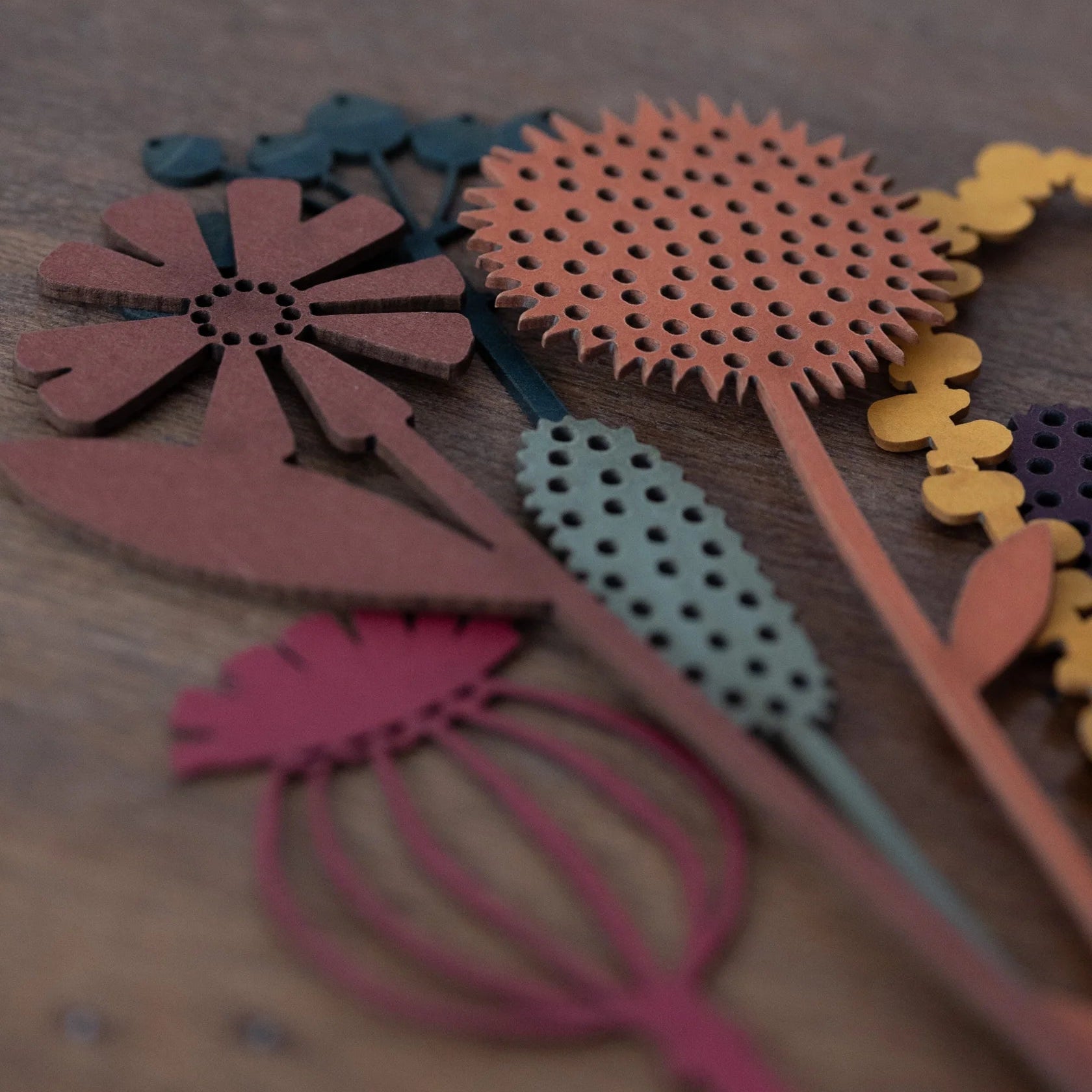 Assortment of laser-cut floral shapes in various earthy tones.  Flowers feature intricate detailing and perforated patterns.