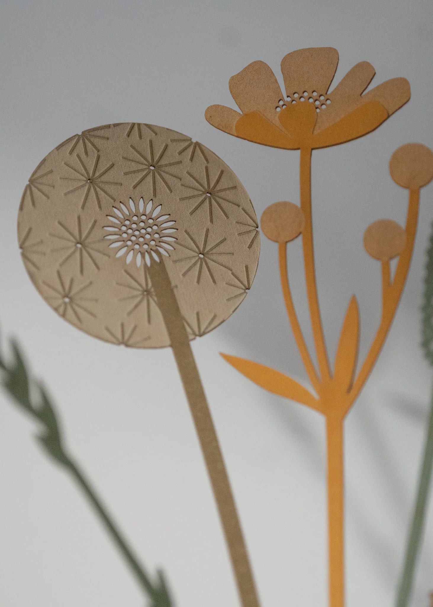 Intricate laser-cut paper flowers; a dandelion-like bloom with radiating detail and a smaller, stylized flower with rounded