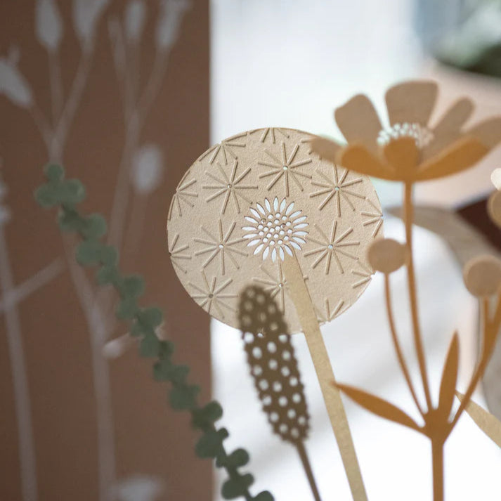 Intricate paper cut-out dandelion clock with radiating starburst pattern and smaller central flower detail.