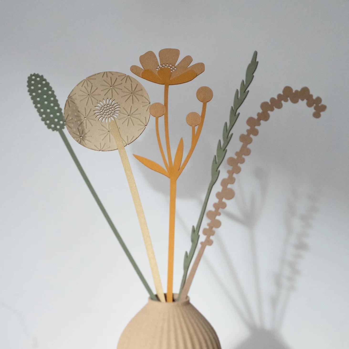 Paper flower diffuser sticks in a beige vase.
