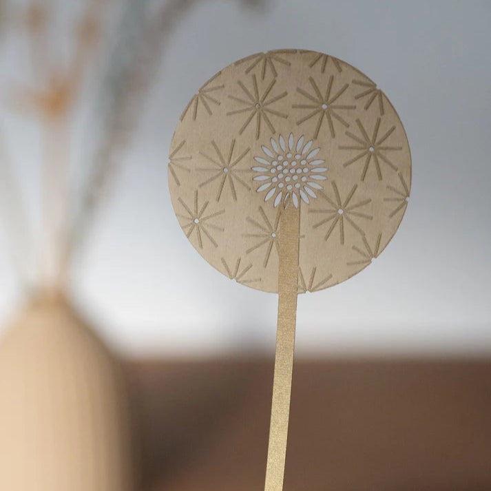 Intricate laser-cut dandelion design, beige cardstock, circular head with detailed seed head and radiating lines.