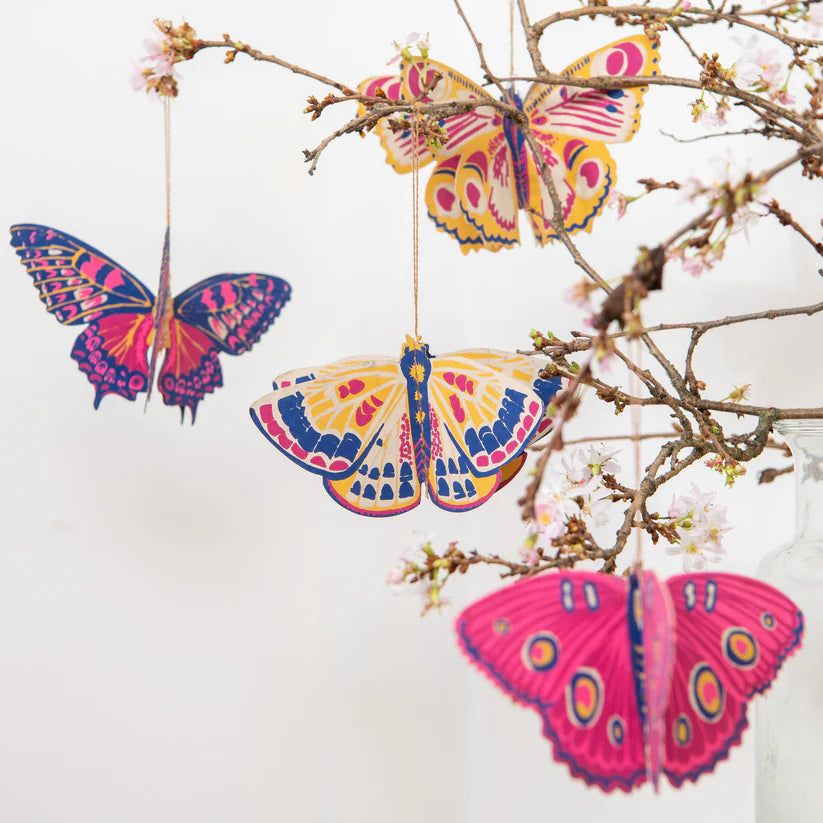 Three colorful paper butterfly ornaments hanging from a branch.  Butterflies feature pink, yellow, and blue designs.