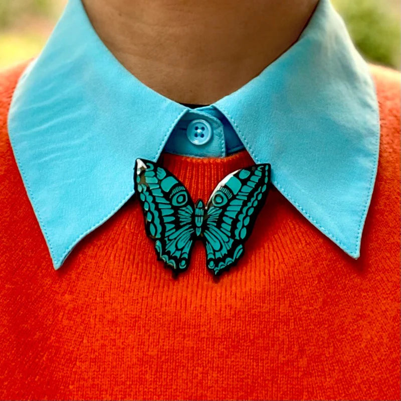Teal and black butterfly brooch on an orange sweater.