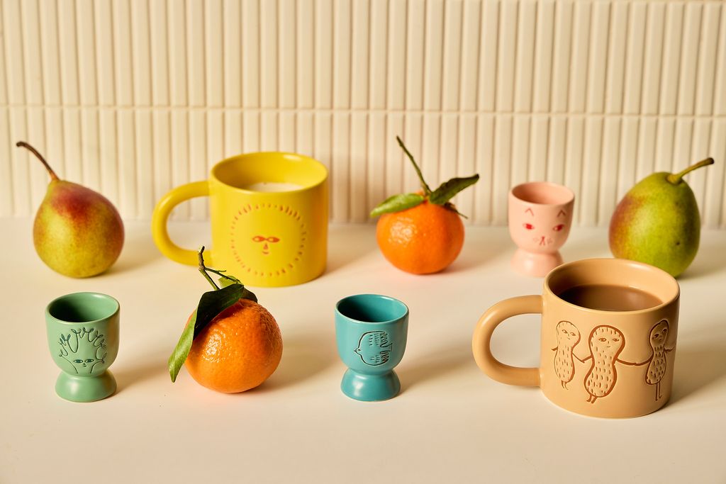 Collection of colorful ceramic mugs and cups with embossed designs on a light background.