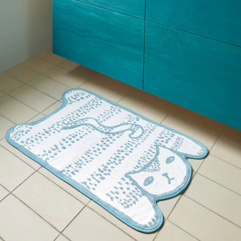 A teal bathroom with a white cat-shaped rug by Donna Wilson, featuring light blue accents and colorful towels.