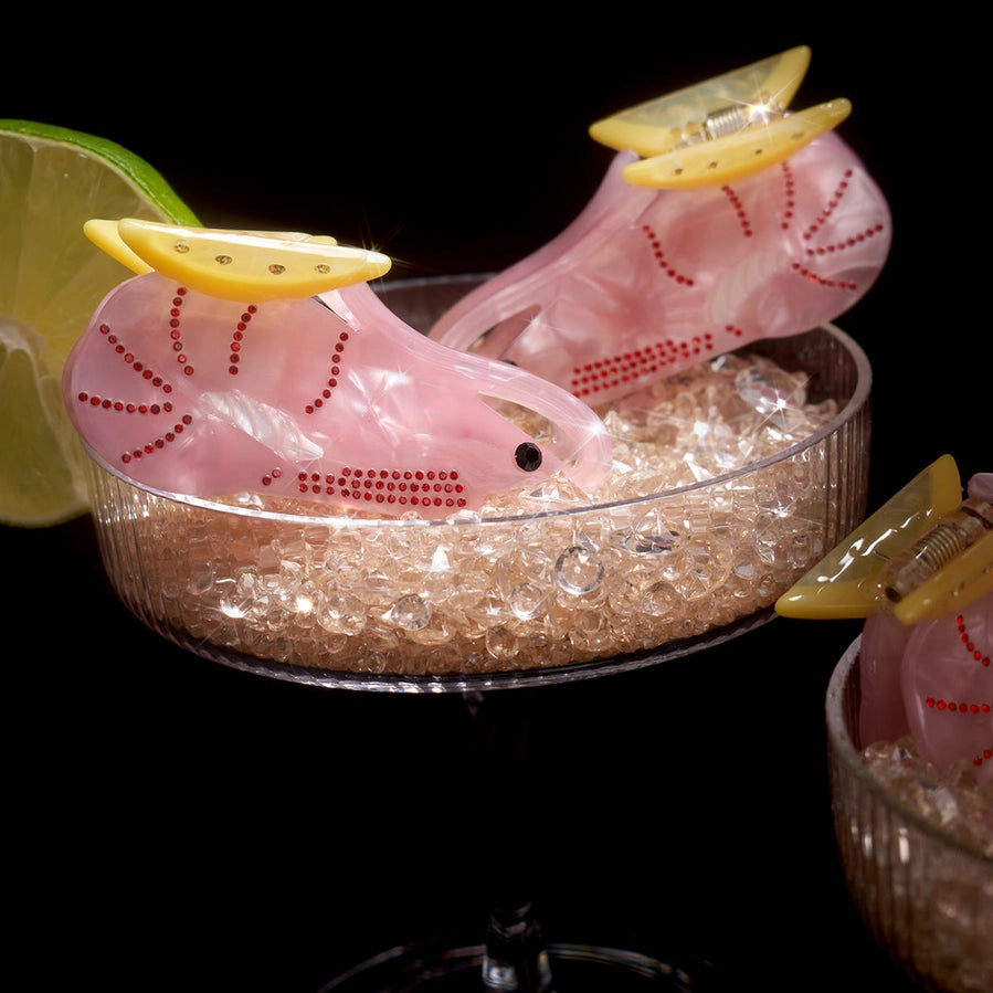 Pink prawns hair clips with lemon slices sit in a glass of ice on a black background
