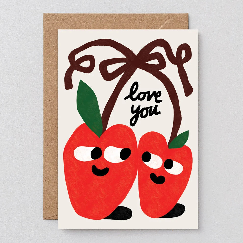 A square greeting card with a kraft envelope behind it, featuring two smiling red apple characters with green leaves and a brown bow above them, with the words 'love you' in black script.