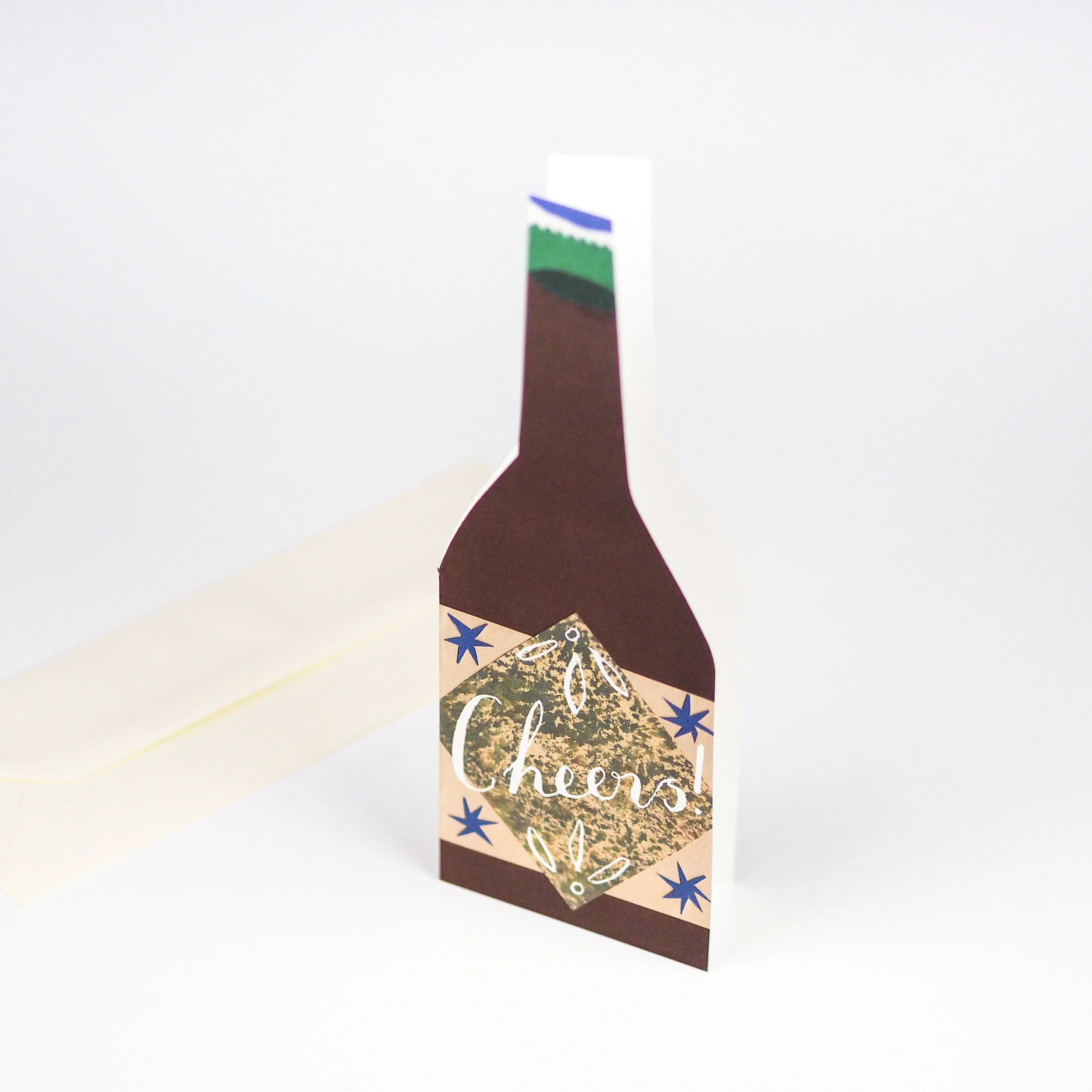 Beer bottle-shaped card with "Cheers!" in white script on a tan and brown design, accented with blue stars.
