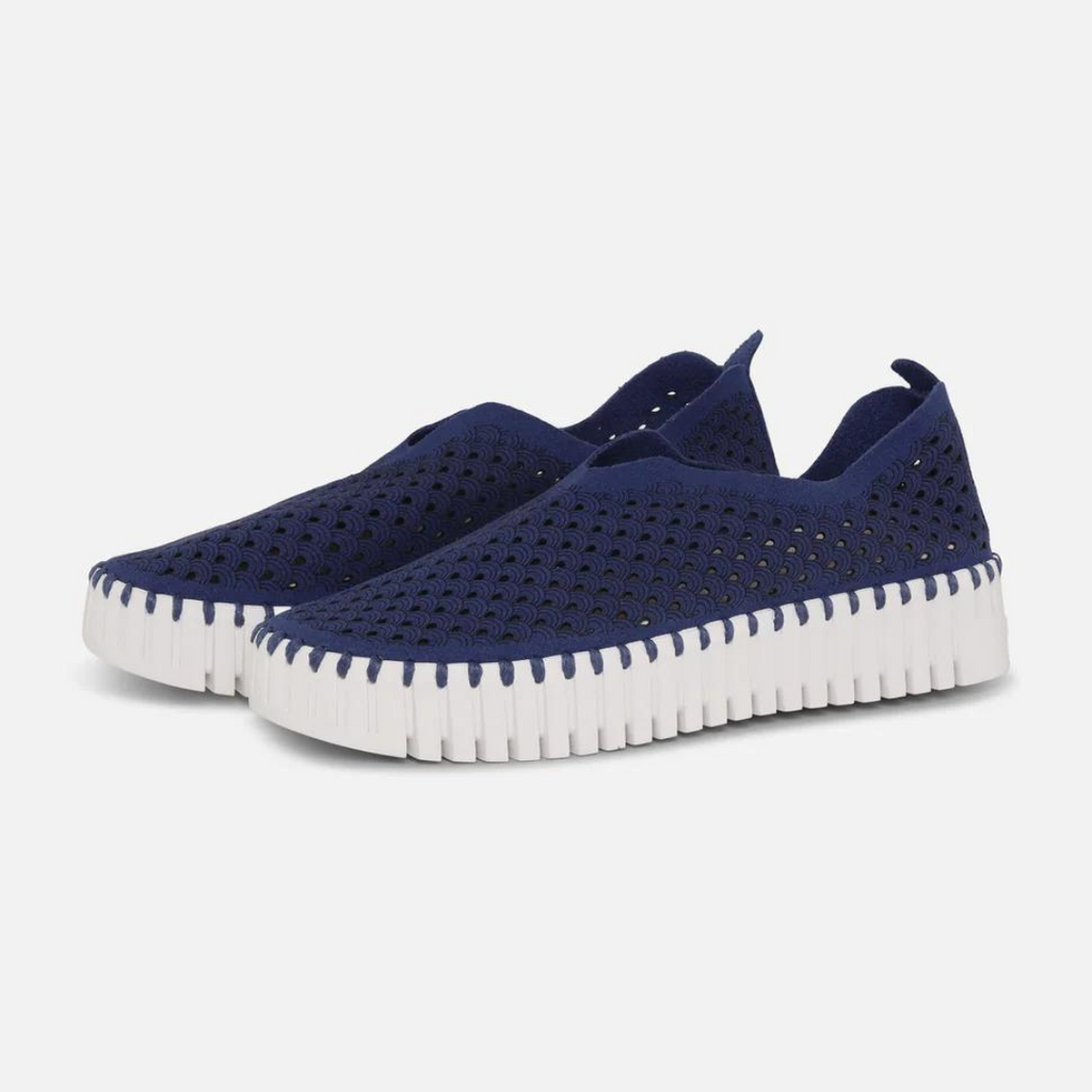 Navy blue slip-on sneakers with white scalloped sole, featuring a textured perforated upper.