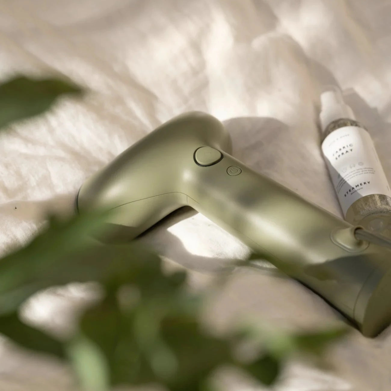 Sage green handheld fabric steamer with a single button.