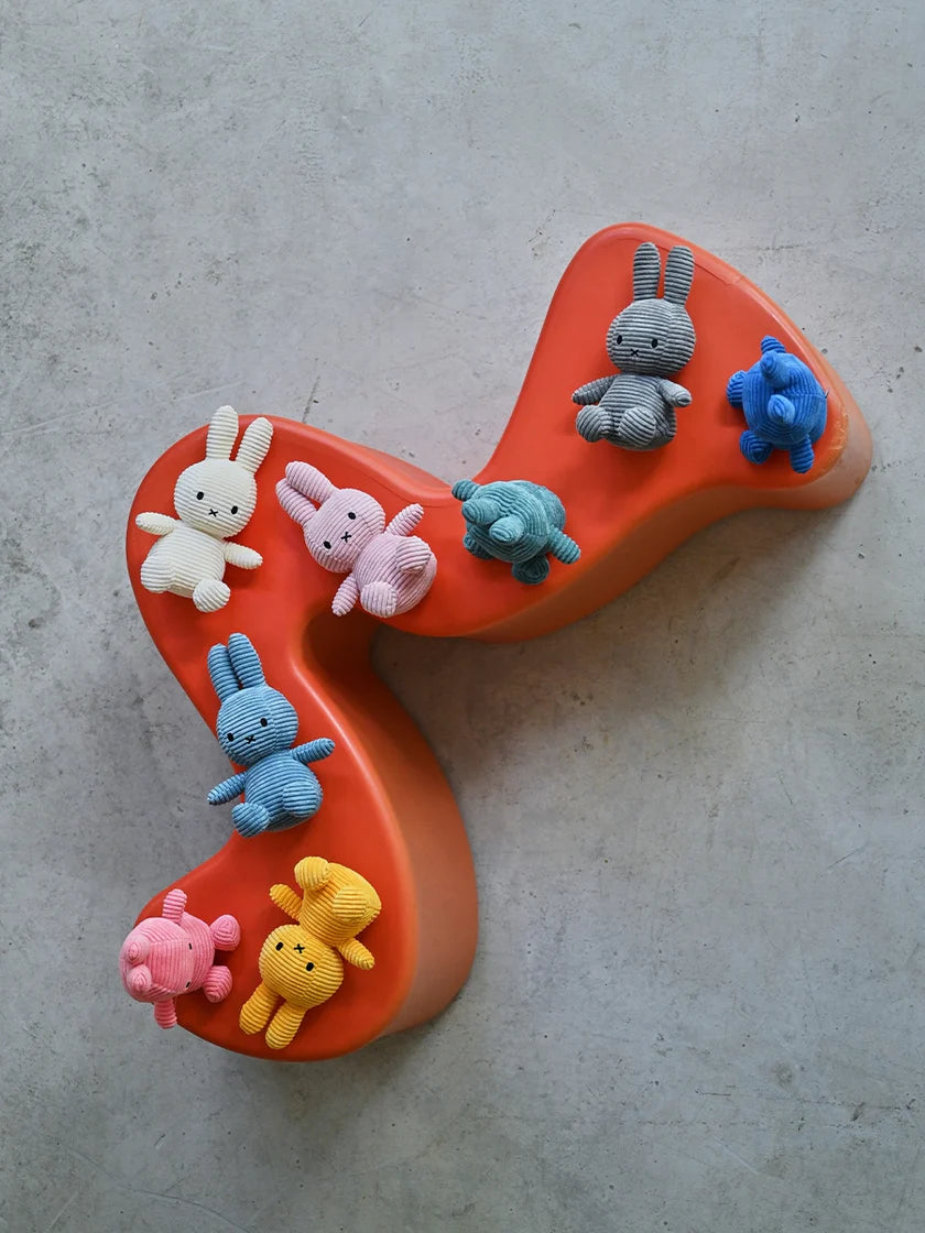 Eight corduroy stuffed animals, including bunnies and bears in various colors, arranged on an orange, curved surface.