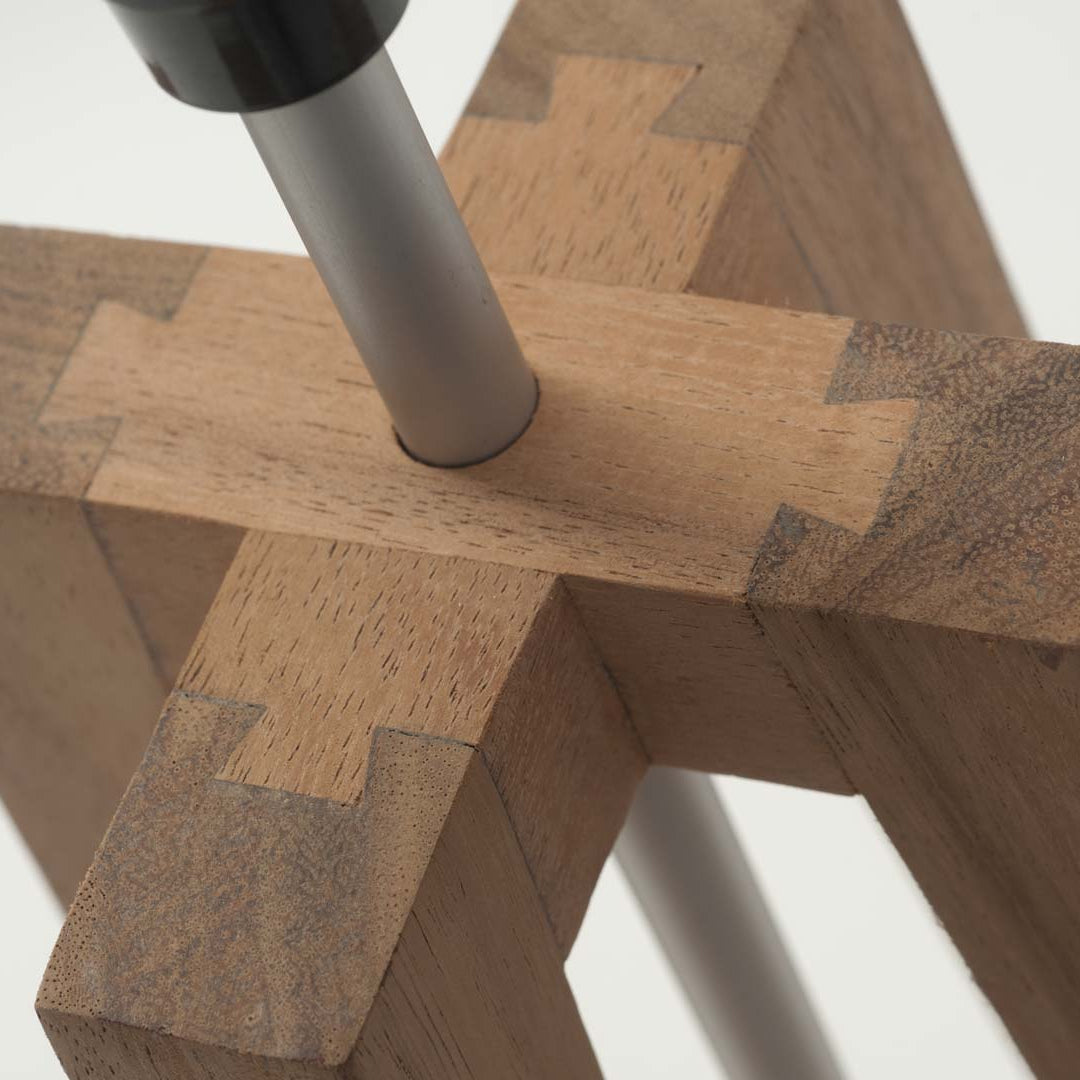 Close-up of a wooden lamp base with a silver metal pole inserted through the center.  The base features intricate joinery.