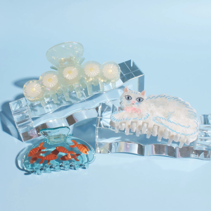Three clear hair clips, one with a cat design, an other with goldfish anf the last with a floral design on a light blue background