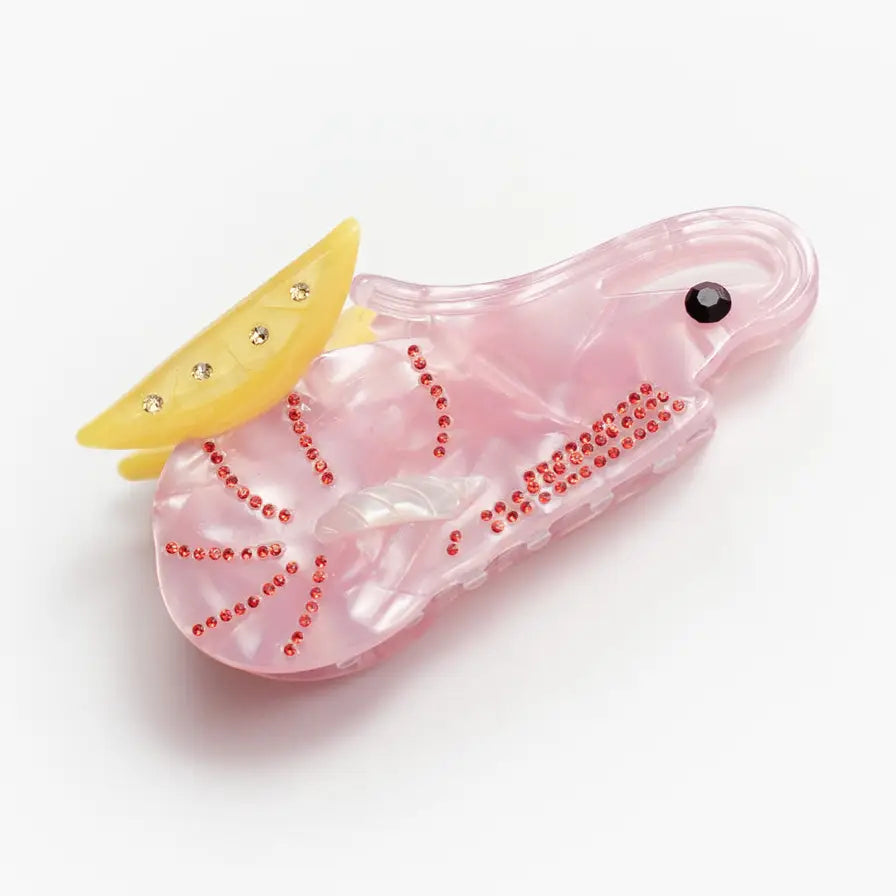 A translucent pink prawn shaped hair clip with rhinestone accents and a yellow decorative lemon wedge, shown on a plain white background.