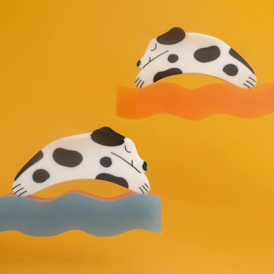 Two dog shaped hair clips with black spots on an orange and blue gradient background