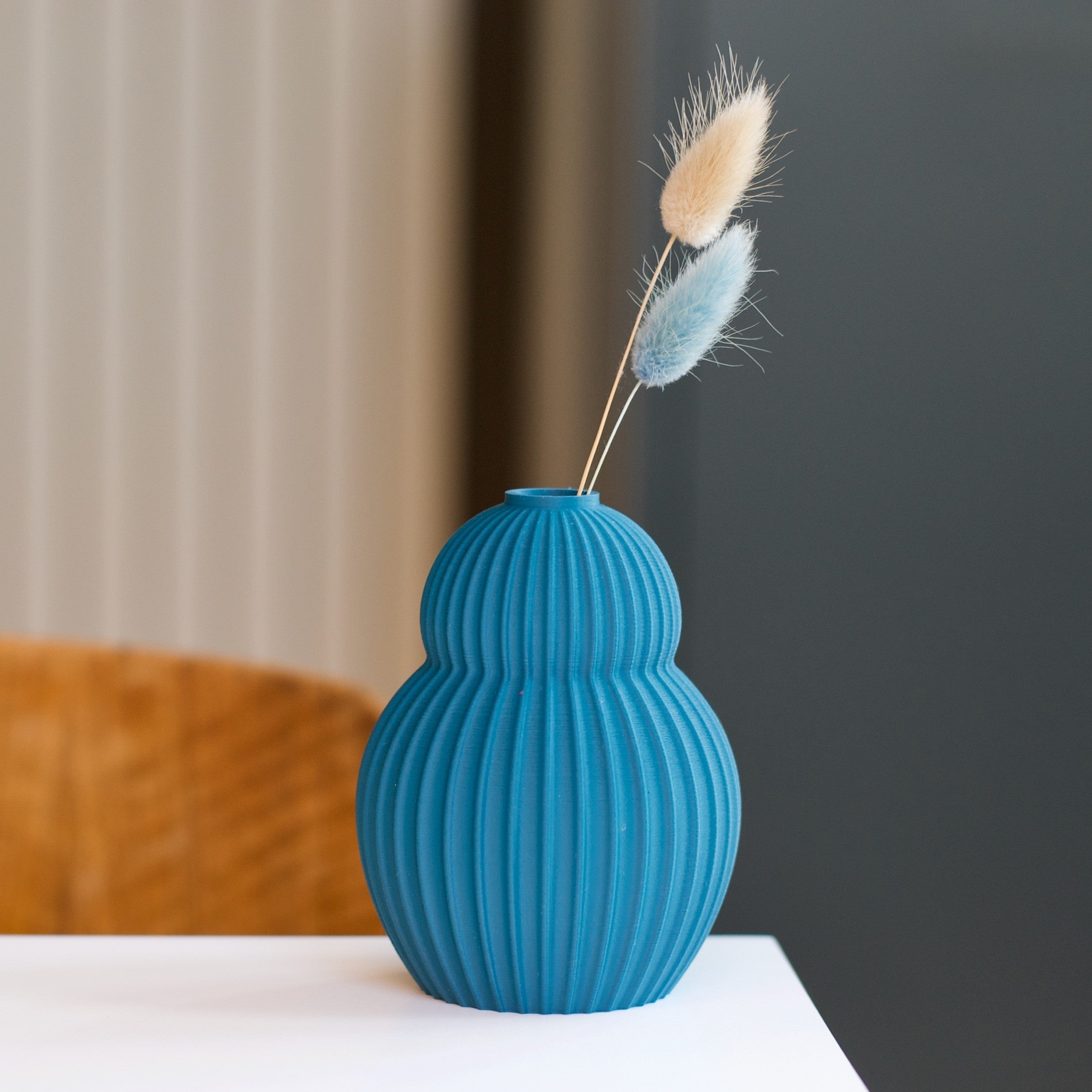 Teal ribbed vase with two dried flower stems; one beige, one light blue.