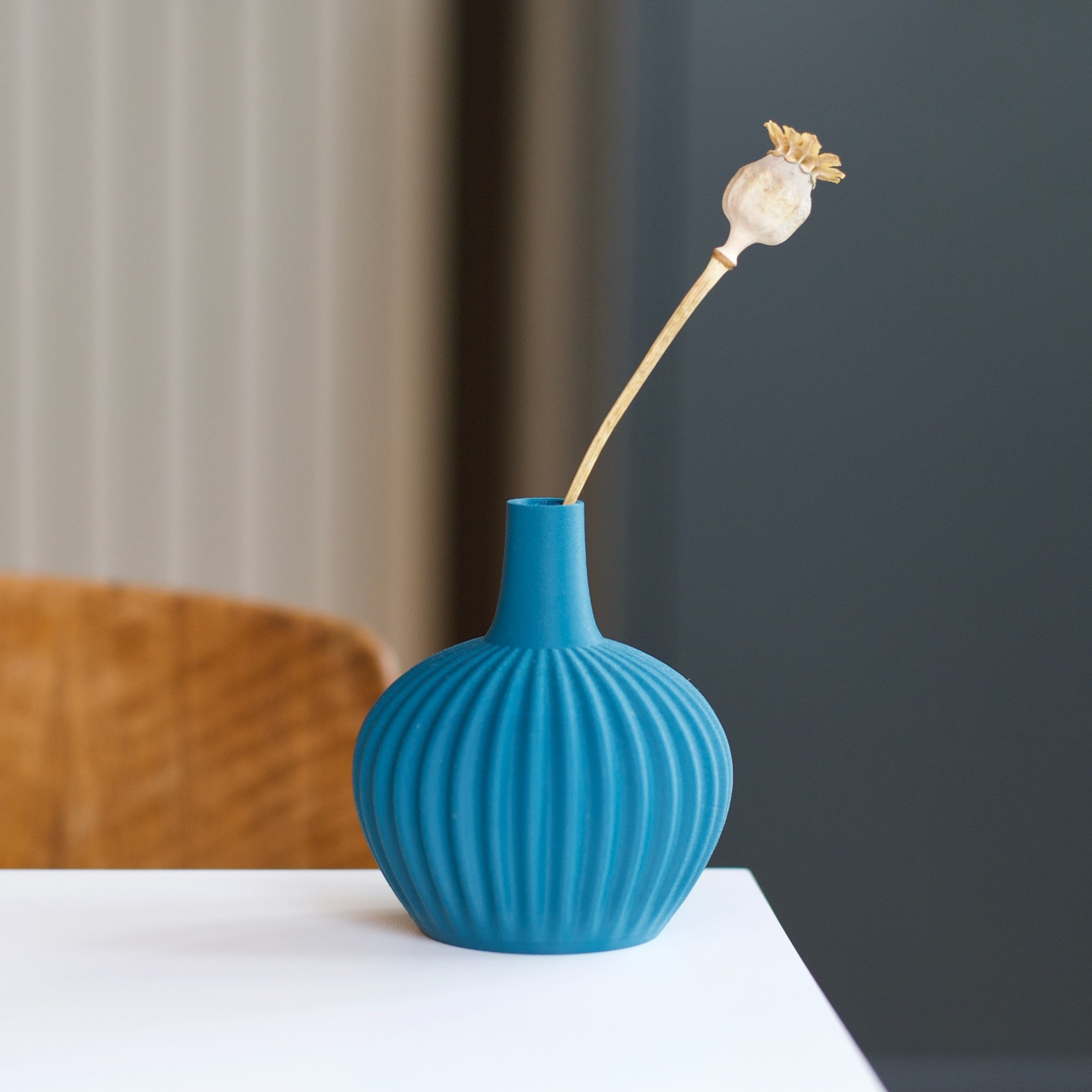 Teal ribbed vase holding a dried poppy seed head.