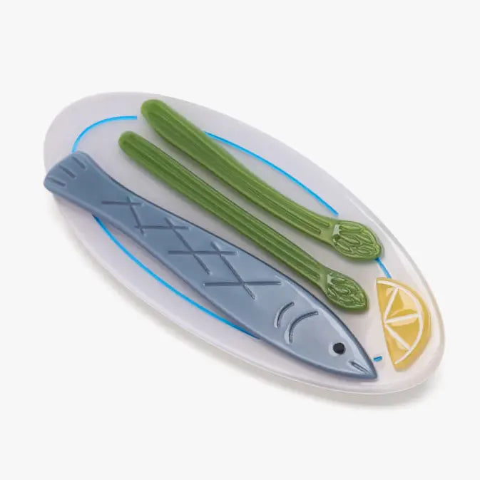 A hair clip with a design featuring a fish, asparagus, and lemon on a white background