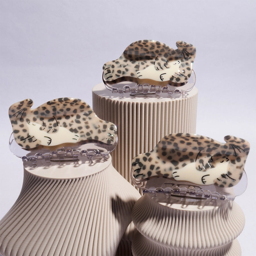 3 hair clips in the shape of seals feature a leopard print design on a beige stand against a light gray background