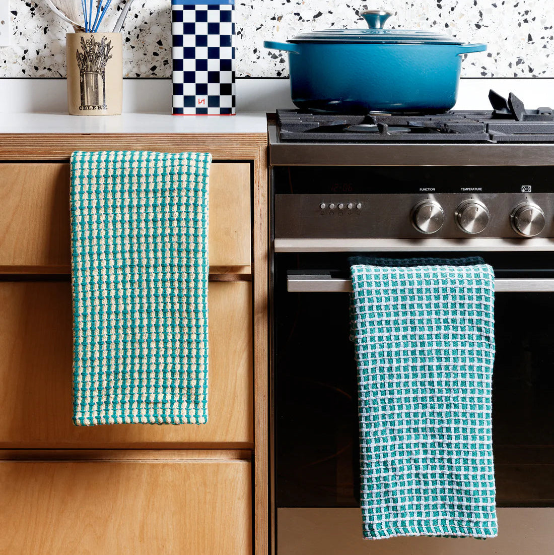Kitchen with wooden cabinets, black stove, and blue pots with green checkered towels hanging on handles.