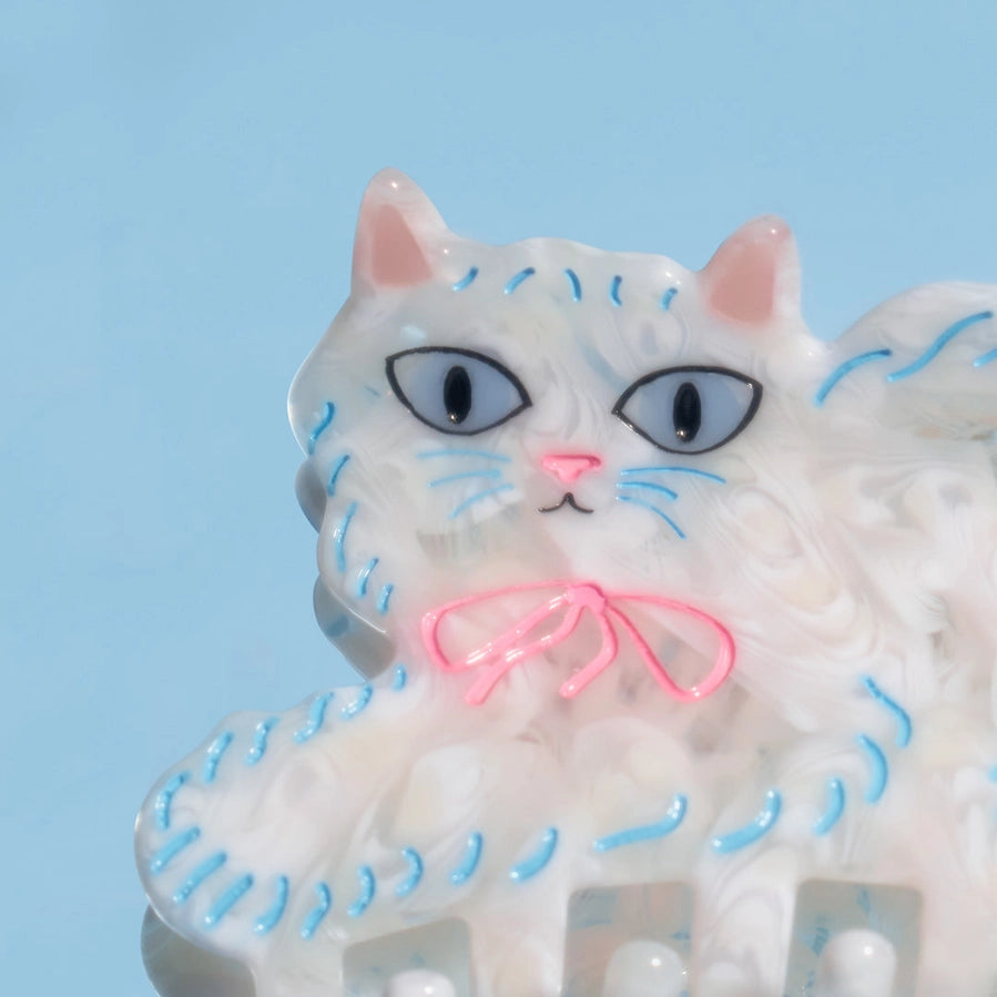 White cat figurine with blue whiskers and a pink bow on a light blue background