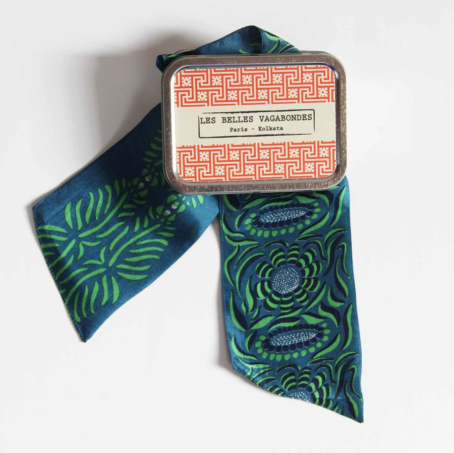 Blue and green patterned scarf with a decorative tin labeled 'Les Belles Vagabondes' on a white background