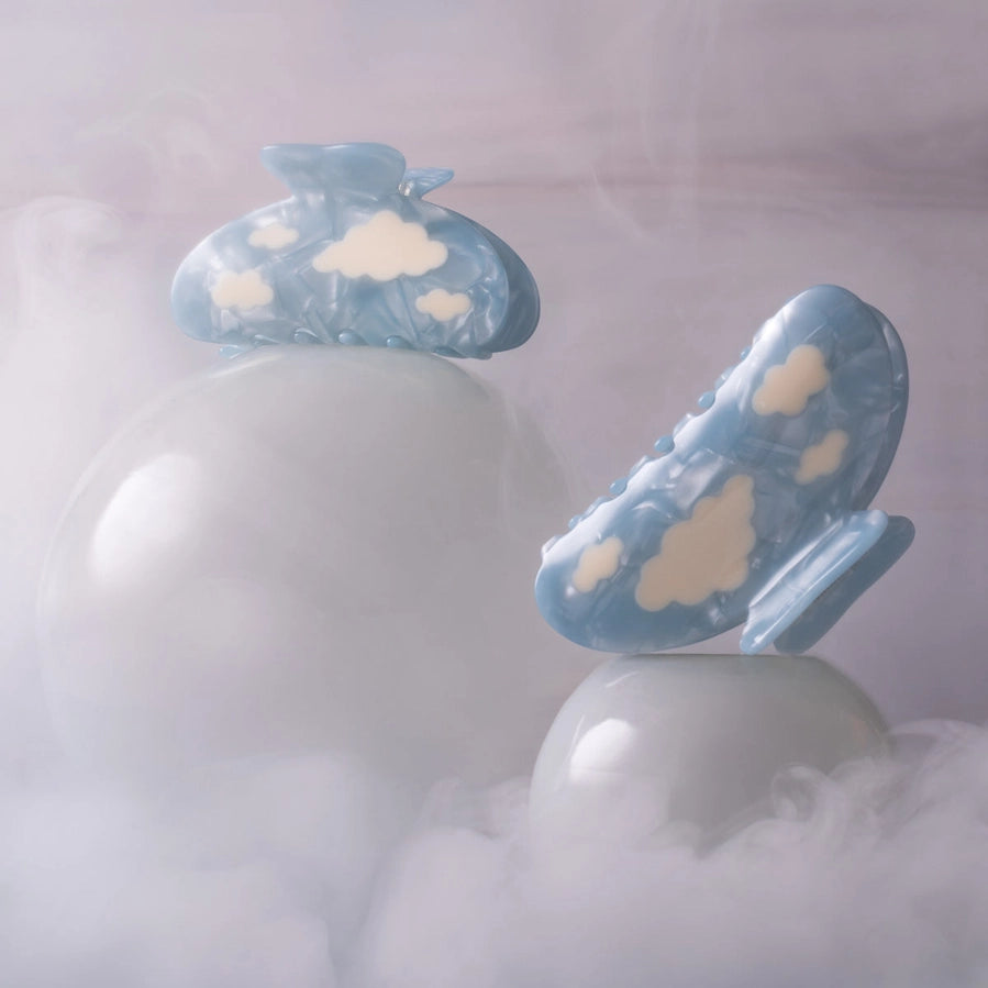 Two blue and white cloud-patterned hair clips on a white pedestal with a soft, blurred background.