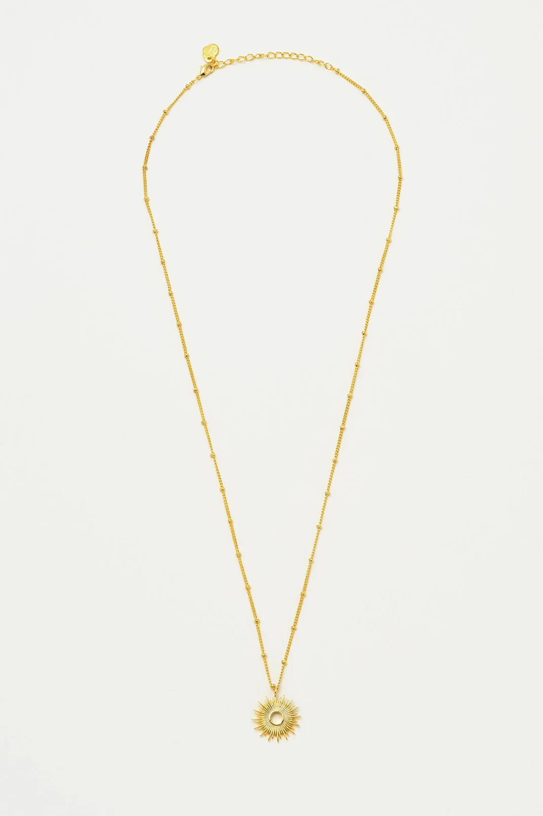 Gold sunburst pendant necklace on a delicate gold ball chain.