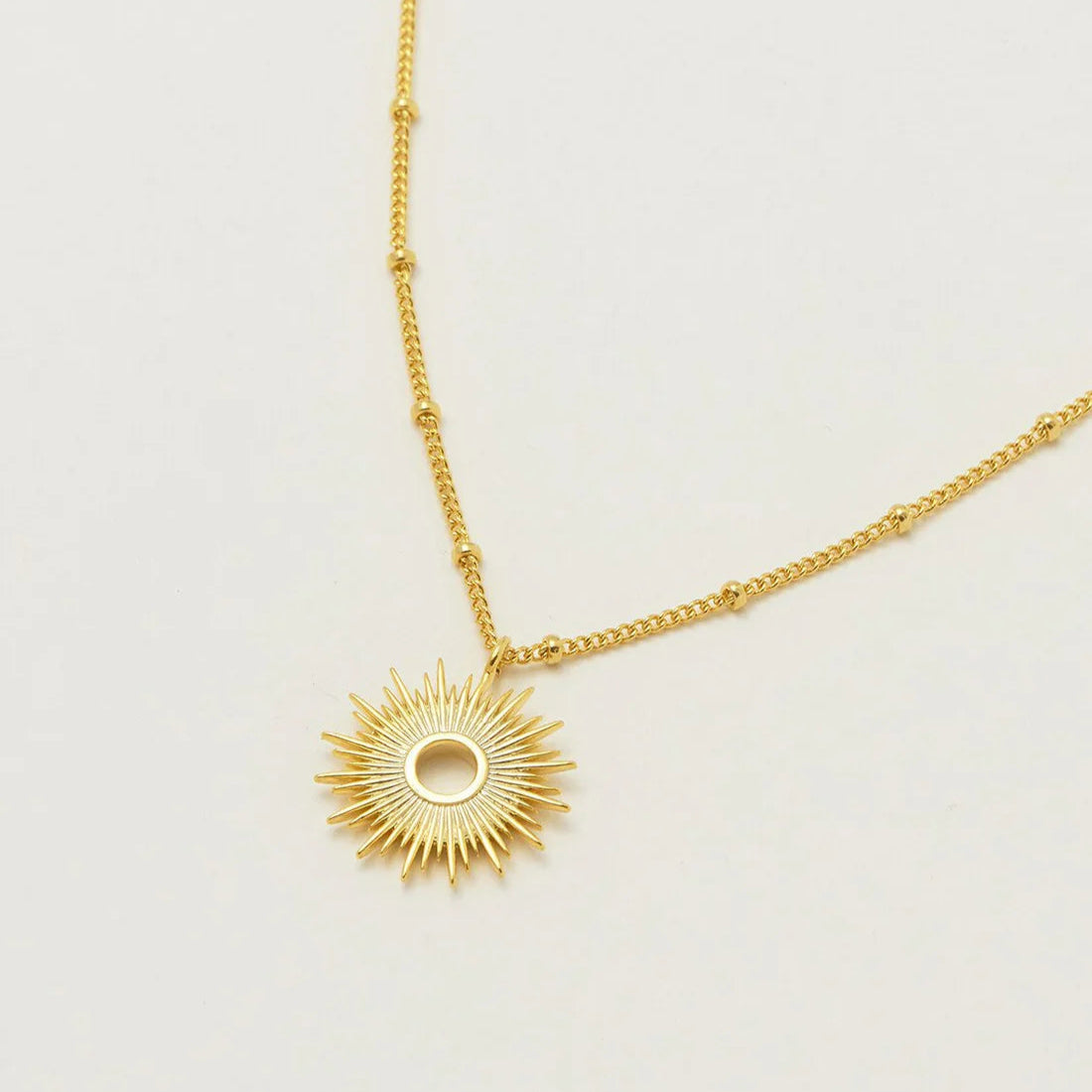 Gold sunburst pendant necklace on a beaded chain.