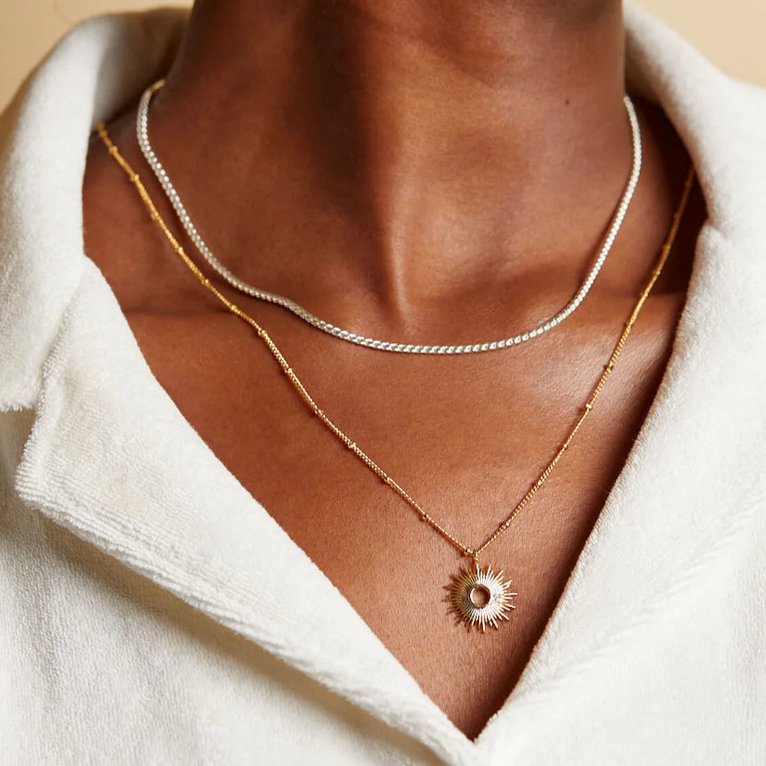 Layered necklaces: a silver chain and a gold chain with a sunburst pendant.