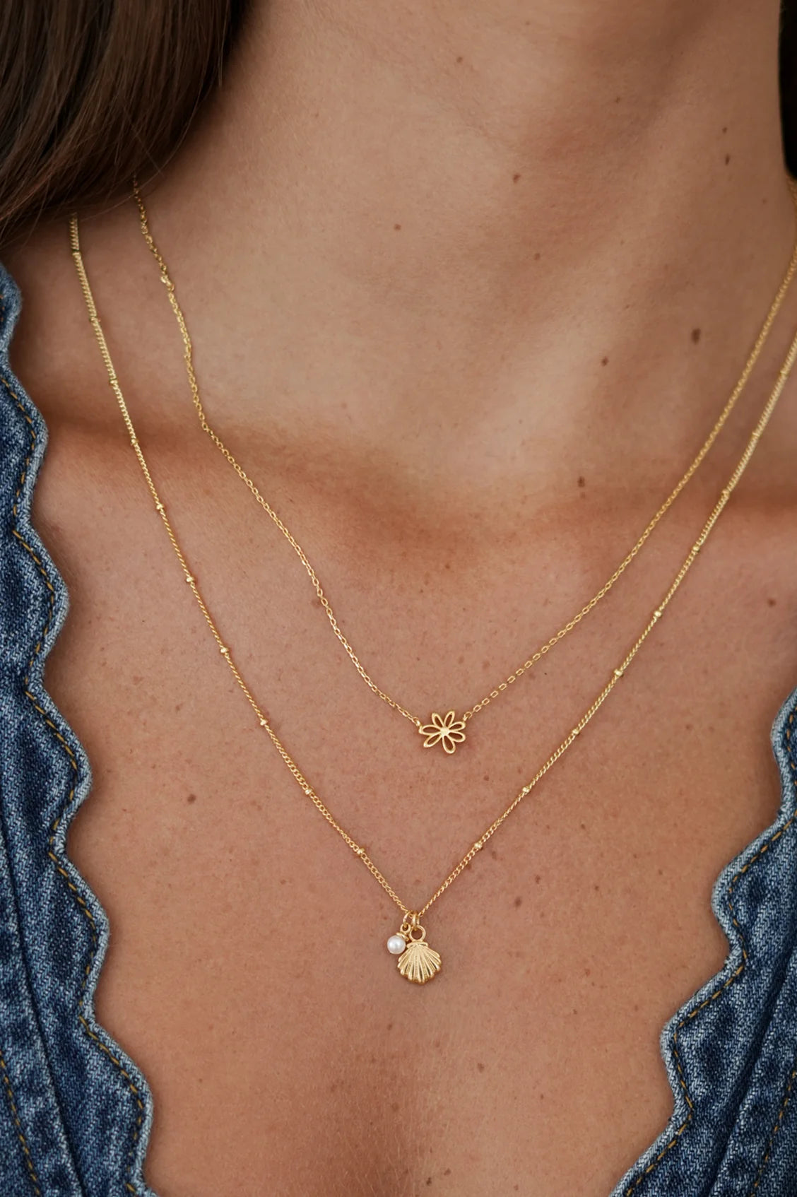Close-up of a person wearing two gold necklaces with floral and shell pendants.