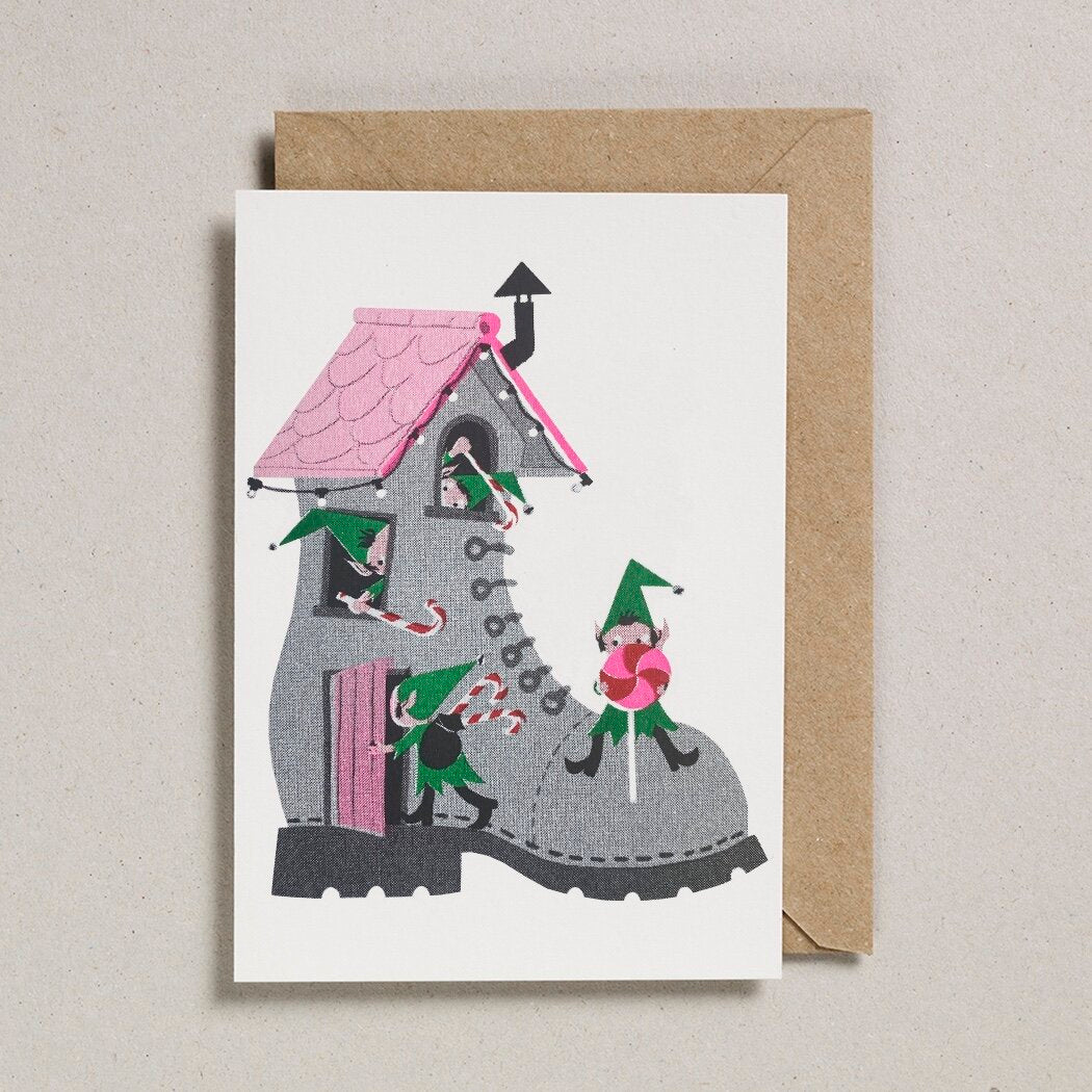 Christmas card depicting a house built inside a large grey boot, with small elves and candy canes.