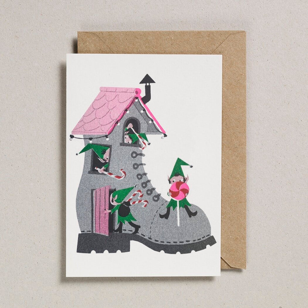 Christmas card depicting a house built inside a large grey boot, with small elves and candy canes.